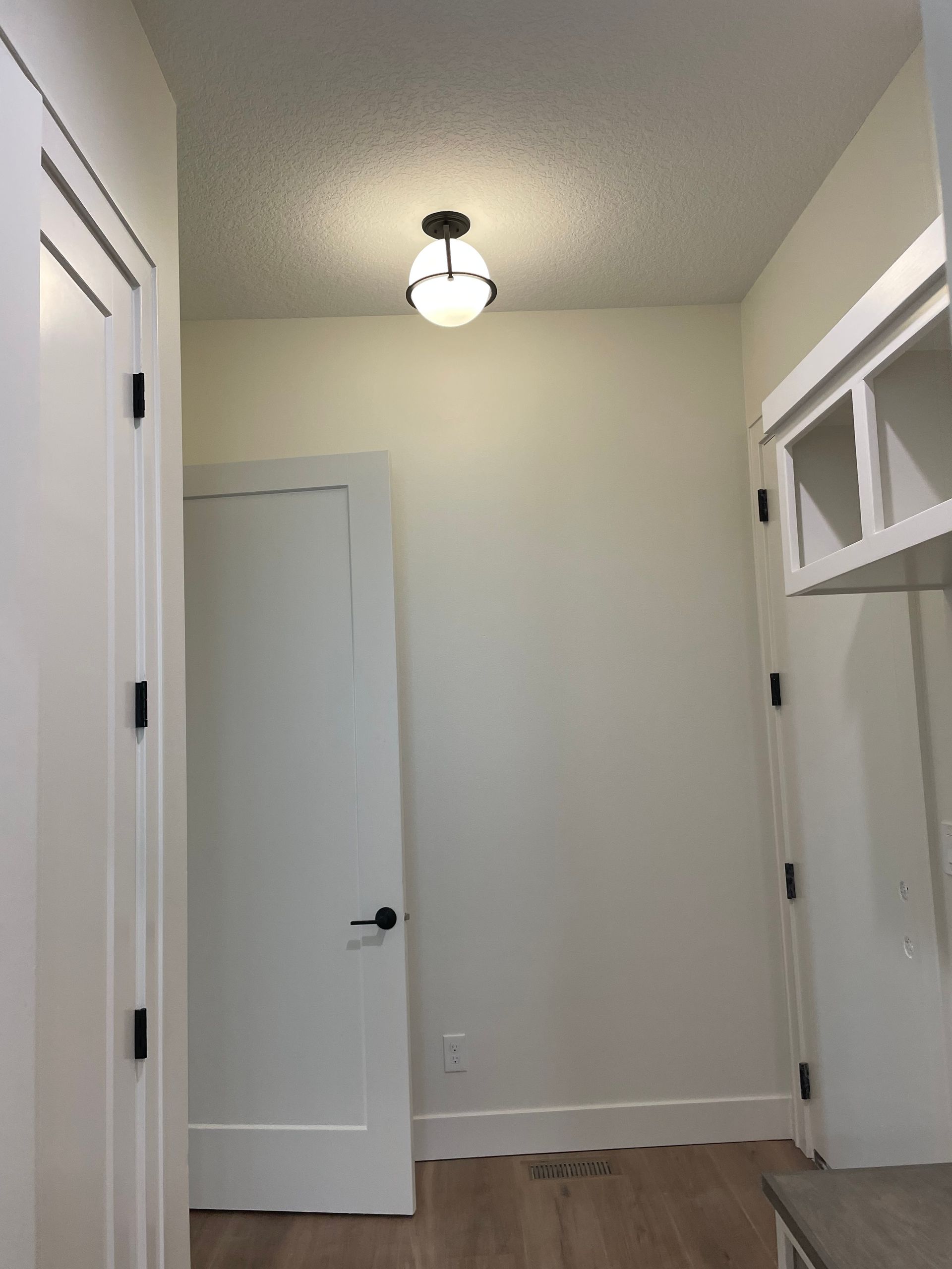 Narrow hallway with white walls, doors, and a ceiling light.