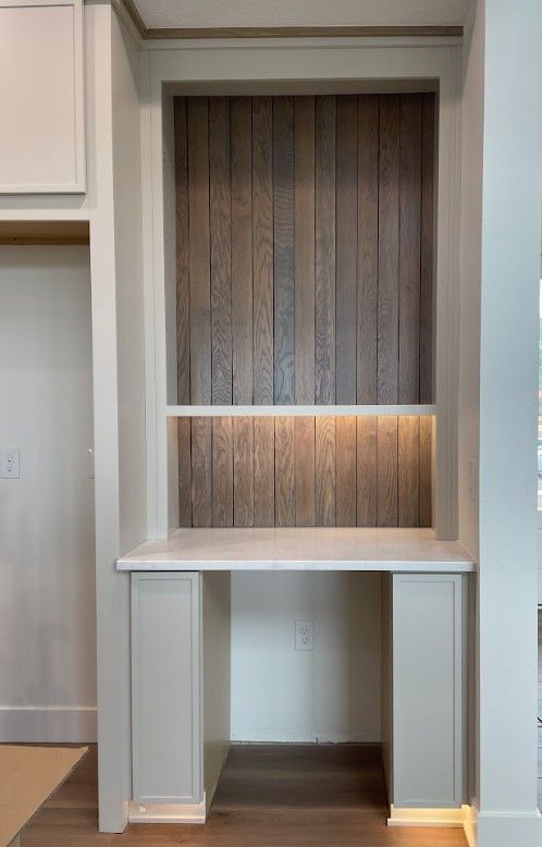 Built-in desk with wooden panel backdrop, shelf, and cabinet doors; lit from above and below.