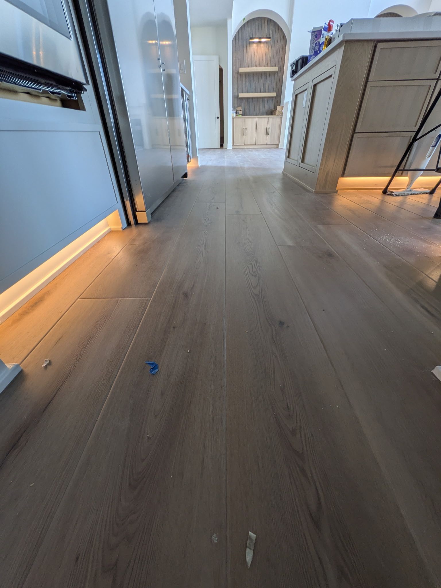 Wooden floor in a bright kitchen with white cabinets, light fixtures, and a distant arched doorway.