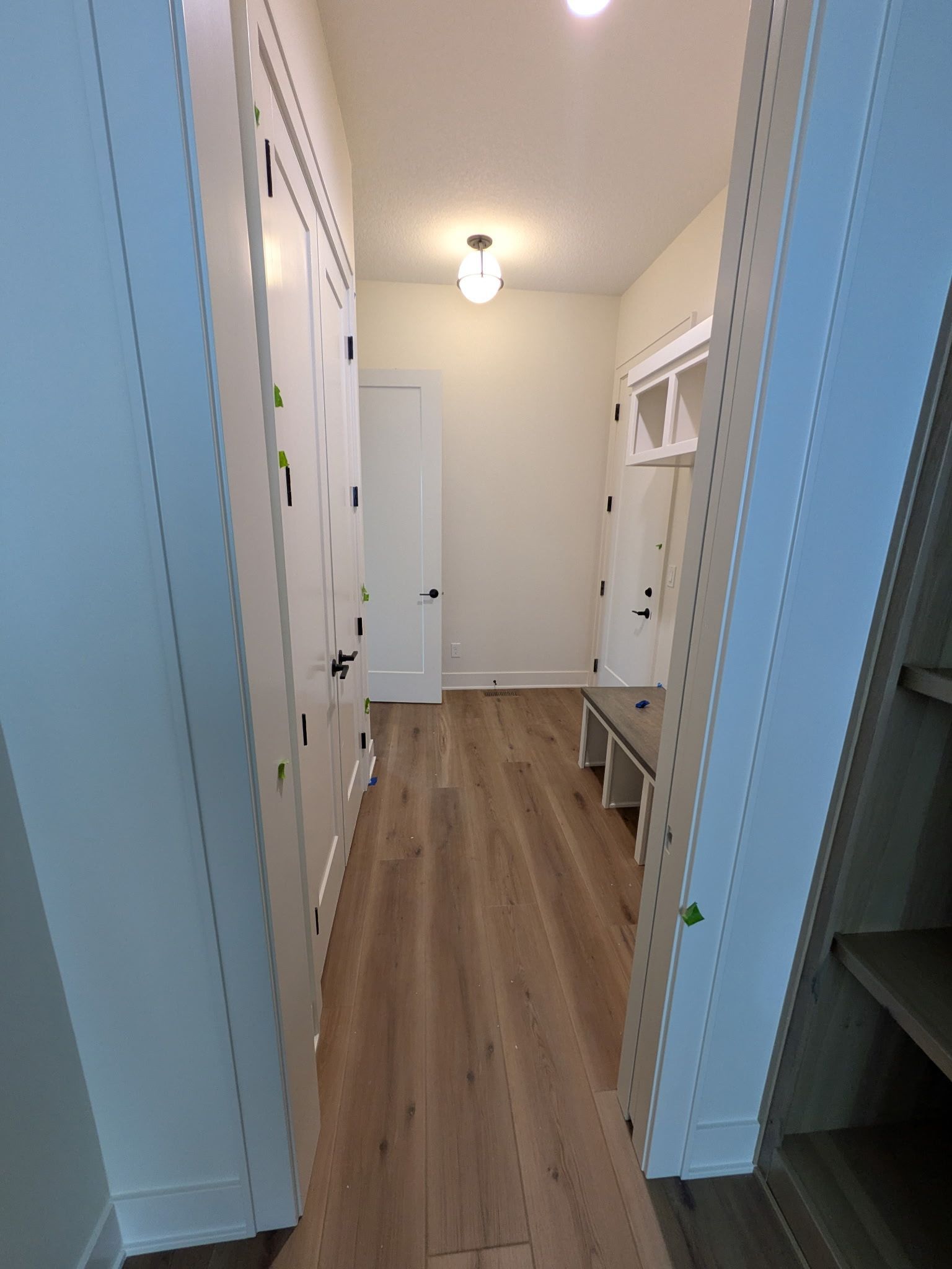 Narrow hallway with white cabinets, light wood floor, and doorway ahead.