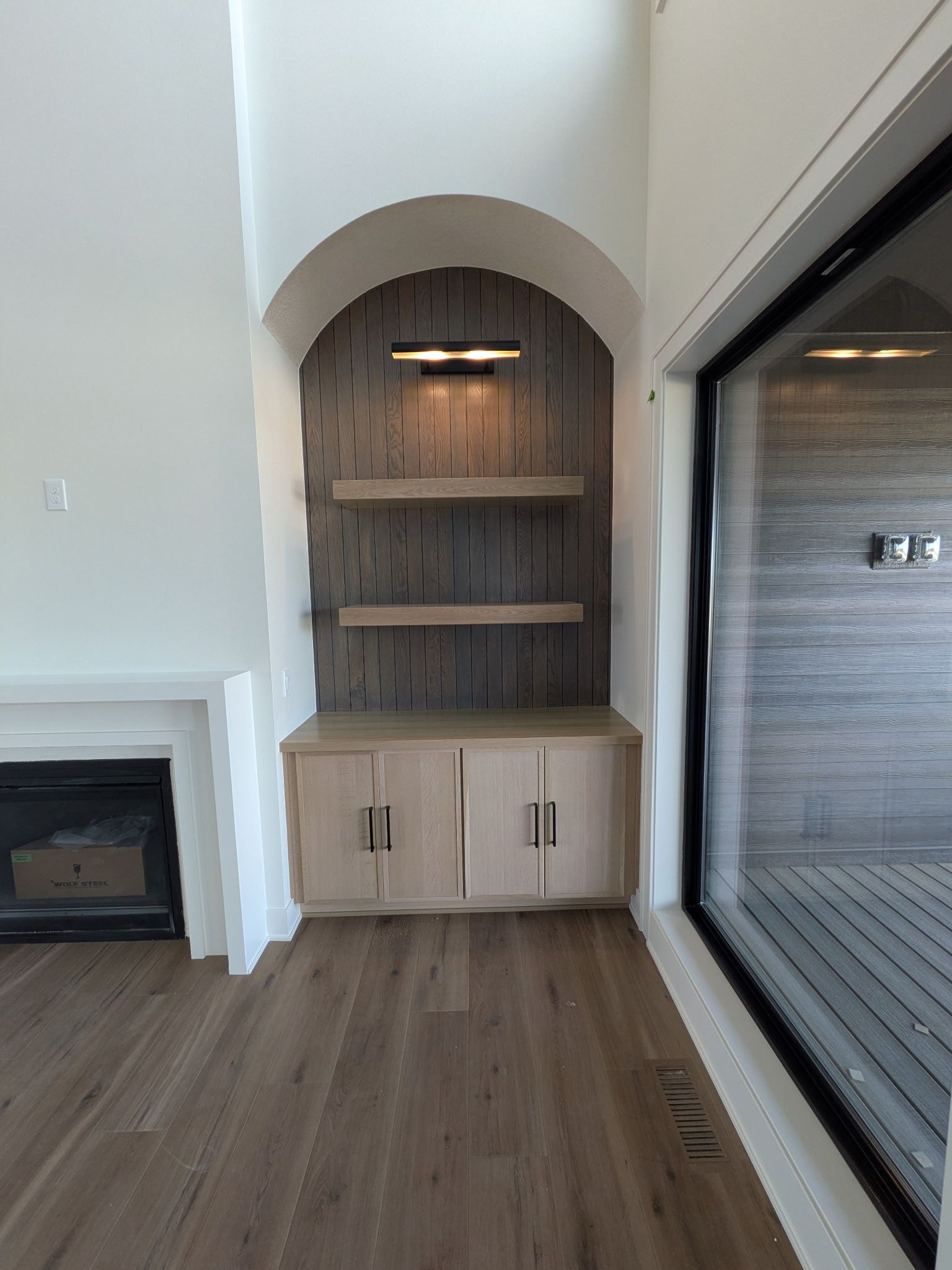 Built-in wooden cabinet with arched top, shelves, and a light in a recessed wall space, next to a fireplace.