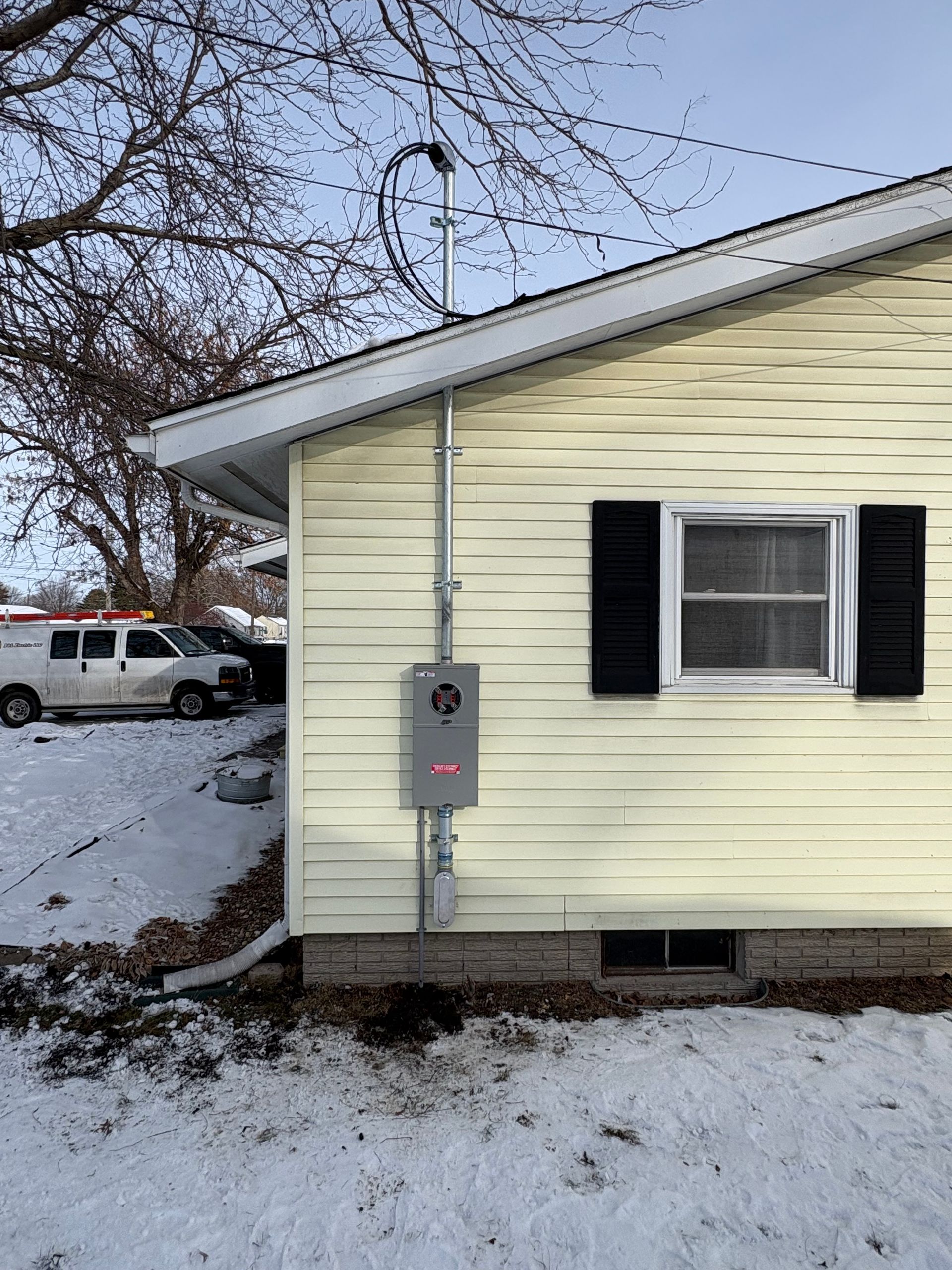 Exterior of a house with an electrical panel on the wall, utility van in the snowy yard.