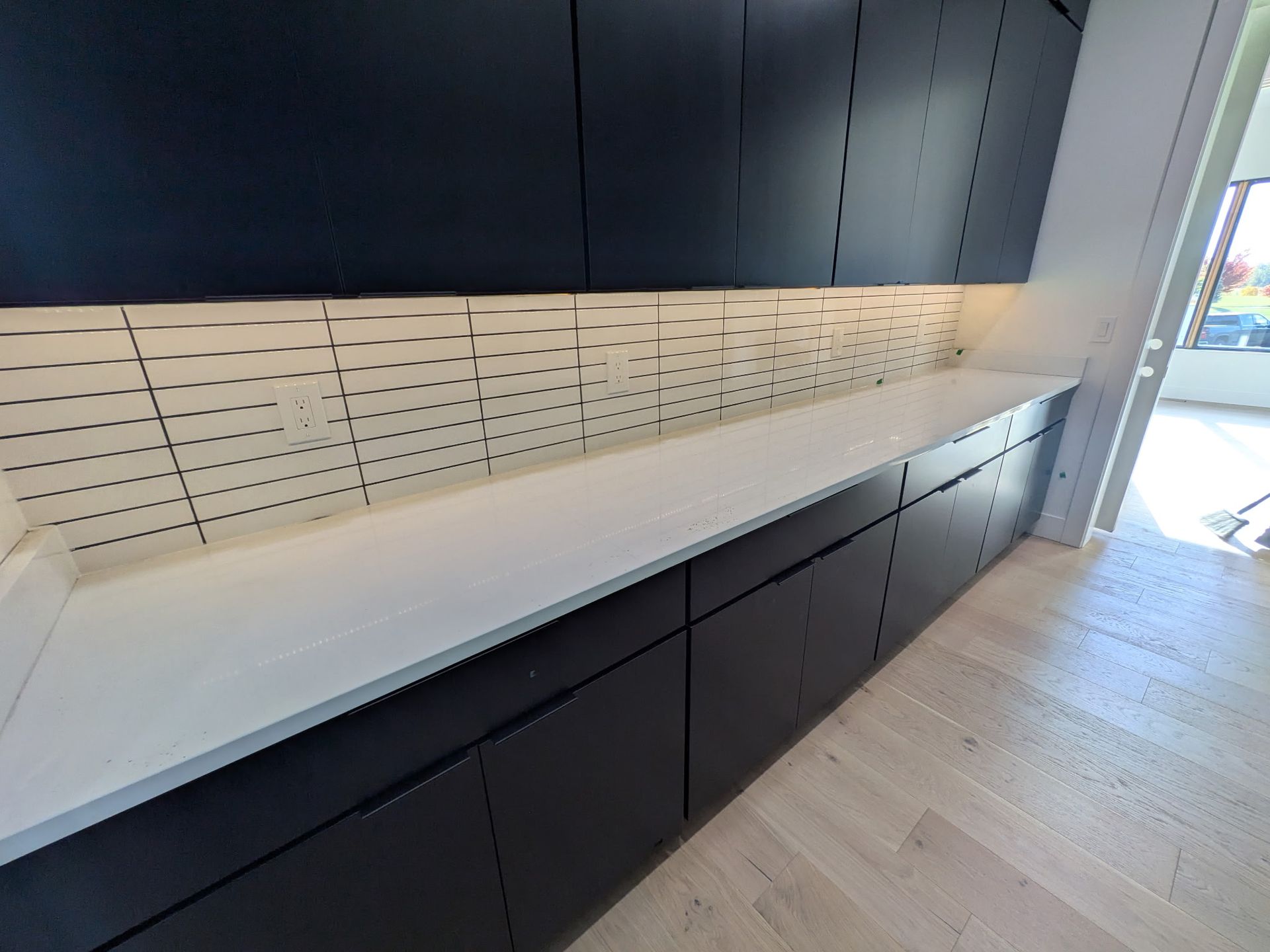 Black kitchen cabinets with white countertop and tile backsplash.