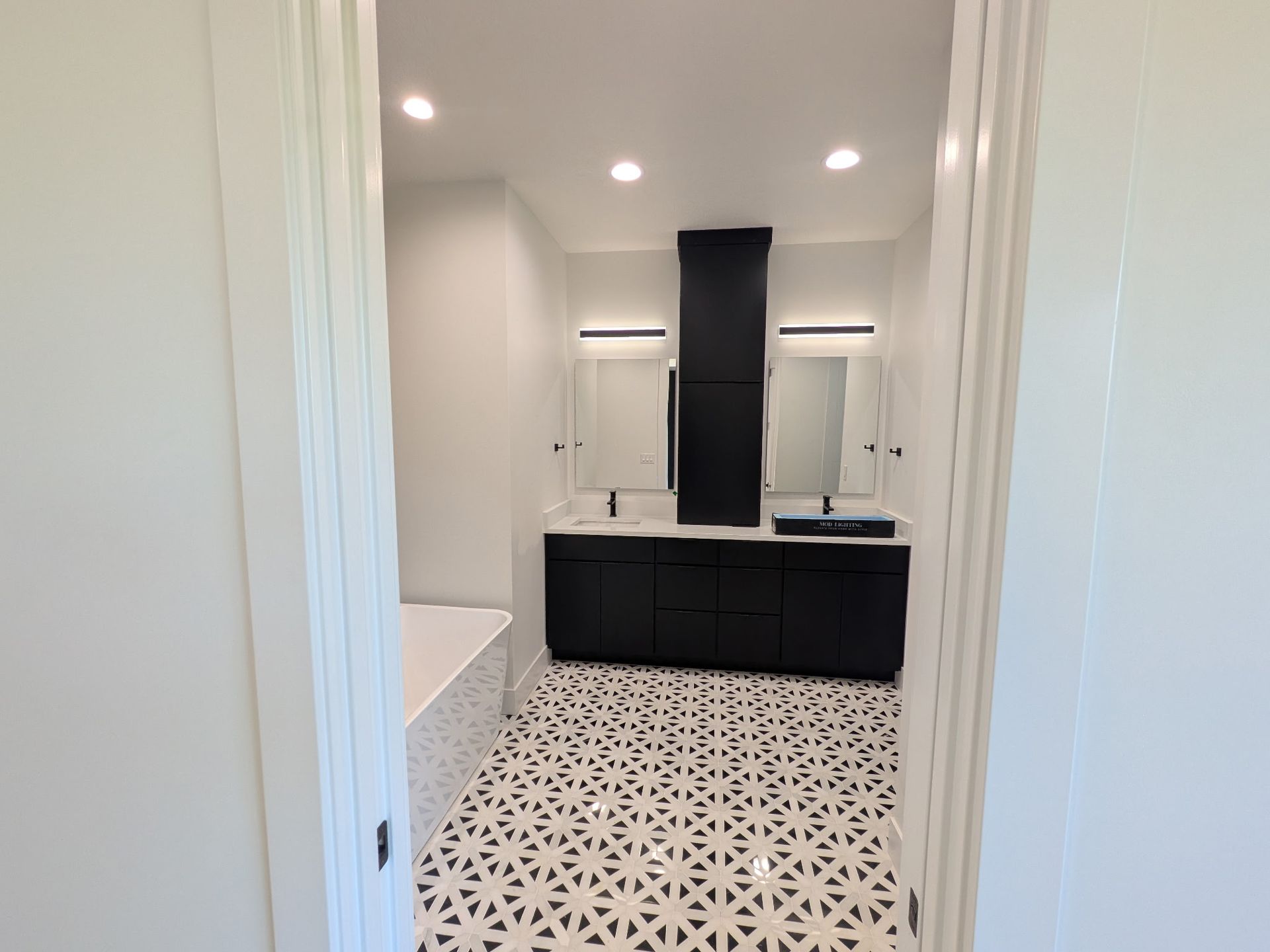 Modern bathroom with black vanity, patterned floor, and tub visible. White walls.