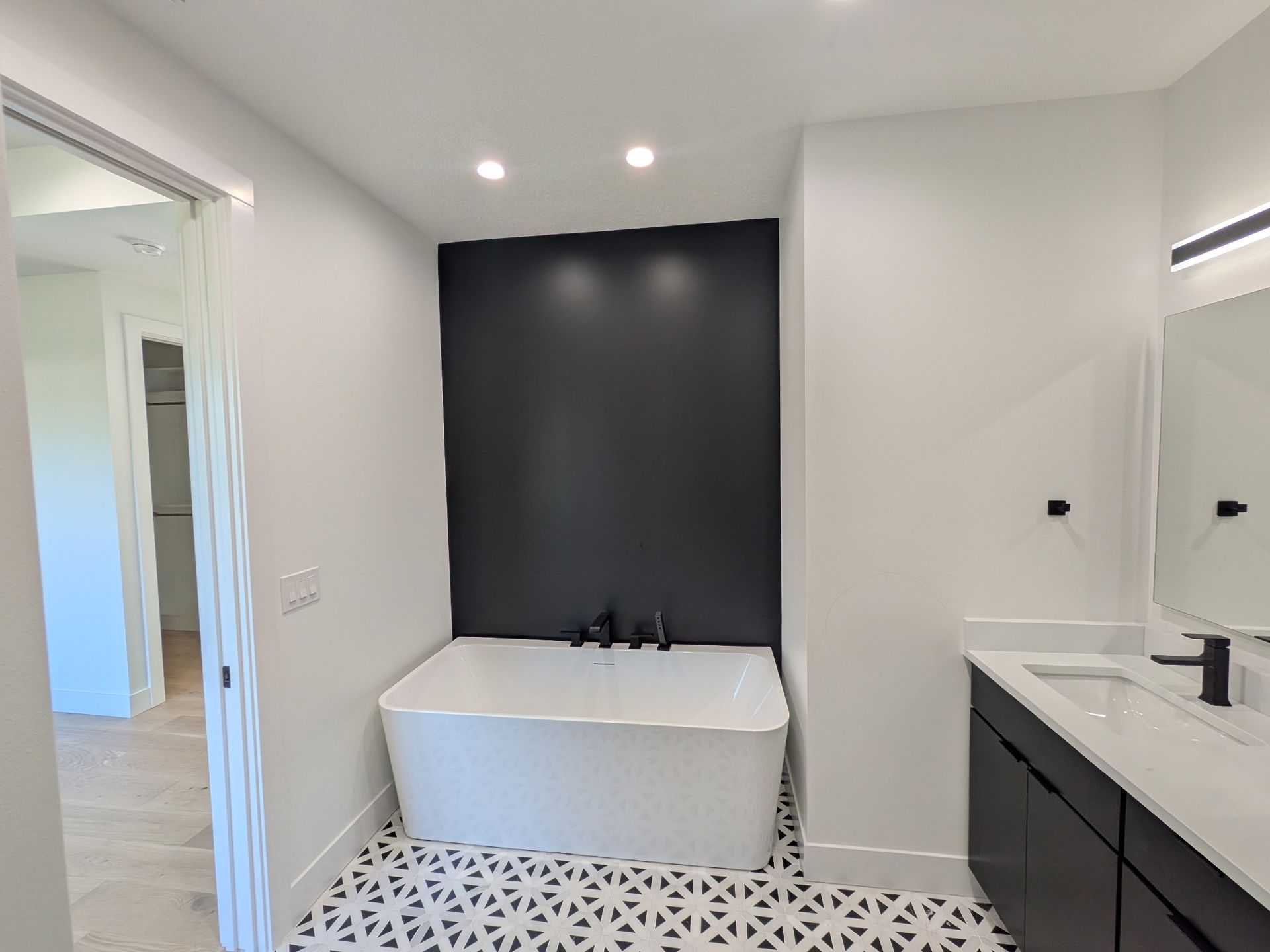 Modern bathroom with black accent wall, white tub, patterned floor, and black fixtures.