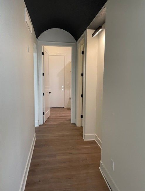 Narrow hallway with white walls, black ceiling, arched doorway, and hardwood floor.