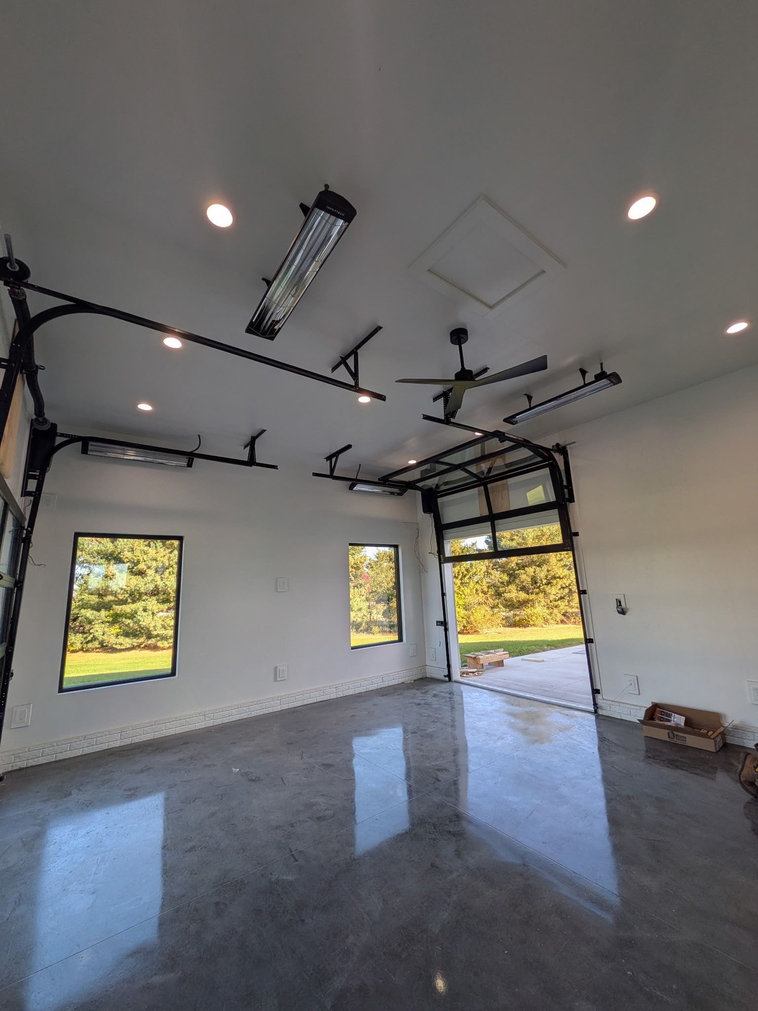 Modern, empty garage with glass doors, windows, and polished concrete floor. Black hardware, recessed lighting.