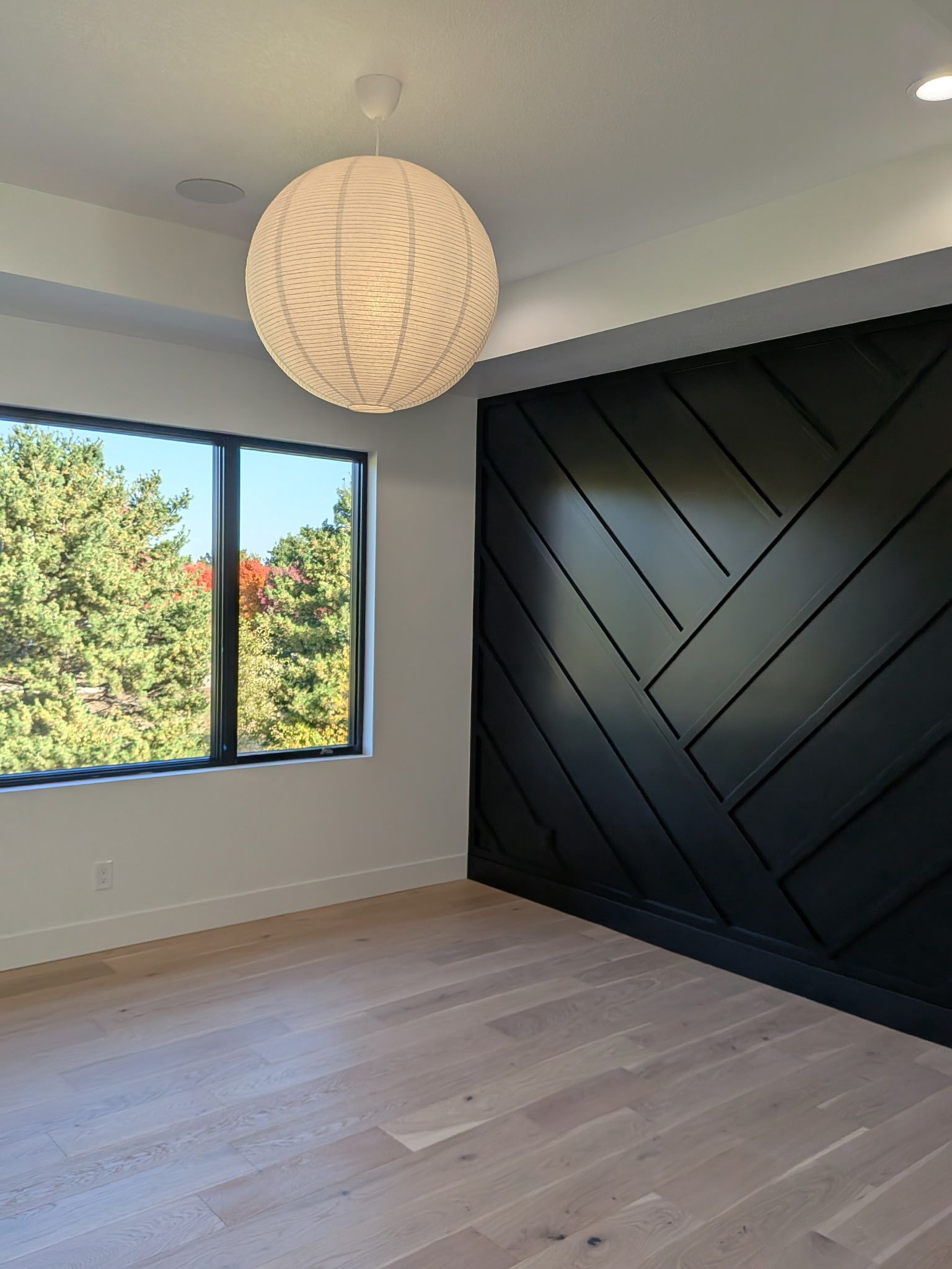 Empty room with black accent wall, window, and wood floors.