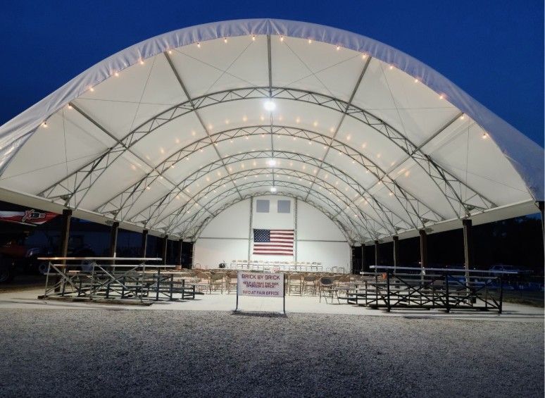 Large white tent at dusk, with string lights and American flag backdrop, containing tables and benches. 