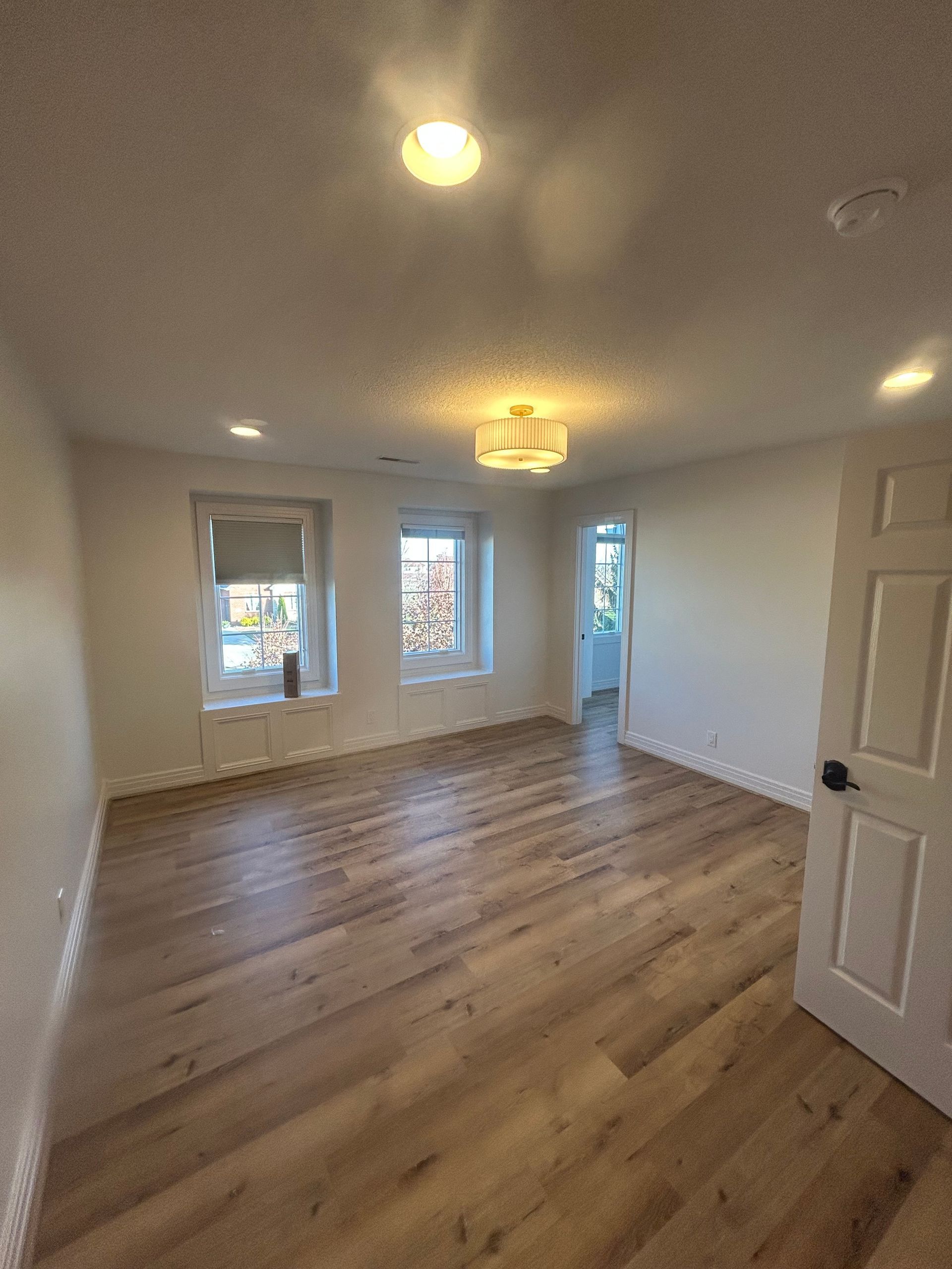 Empty, bright room with wood-look flooring, two windows, recessed lighting, and a doorway.