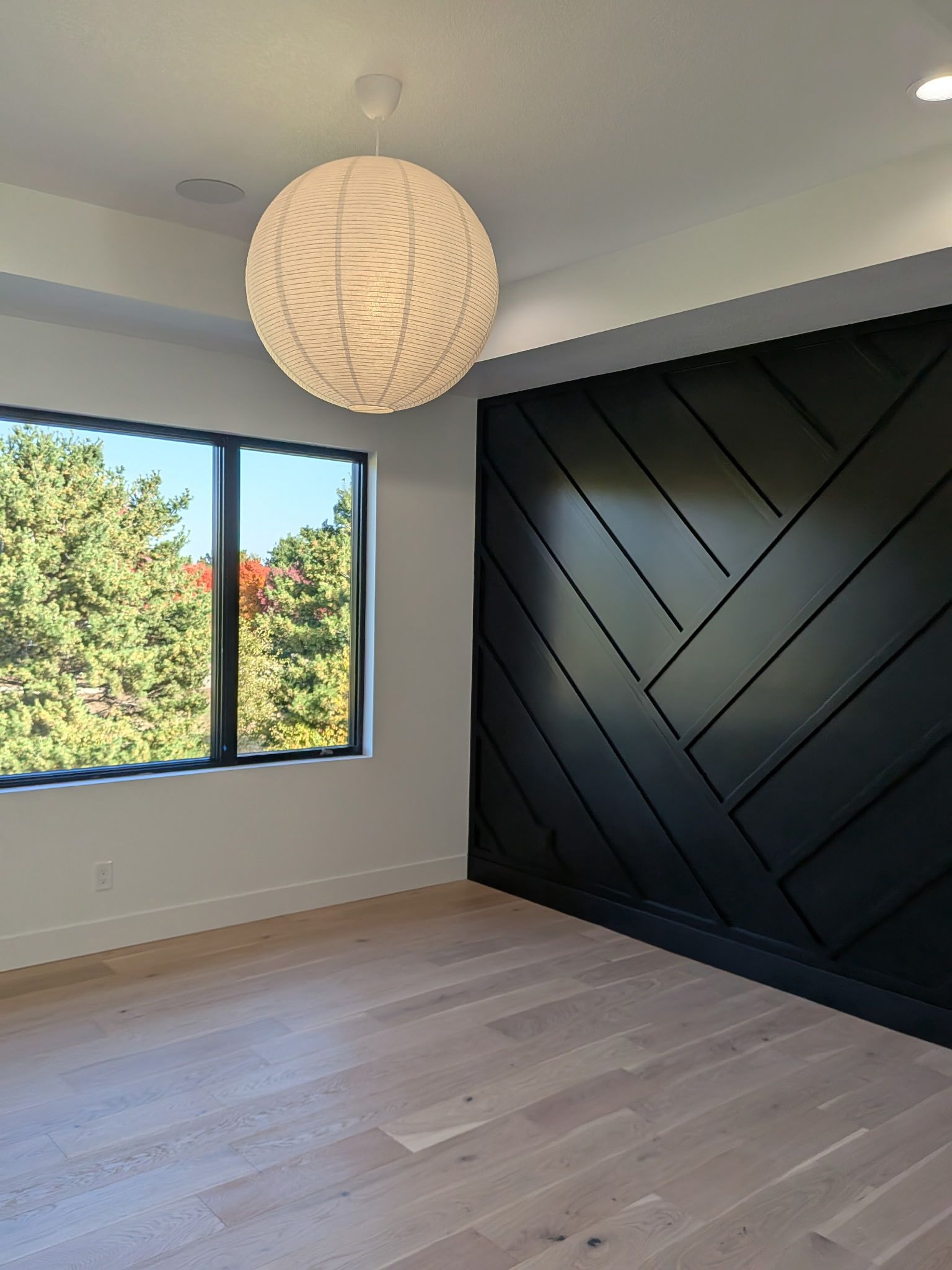 Modern room with black herringbone accent wall, light wood floor, round pendant light, and window.
