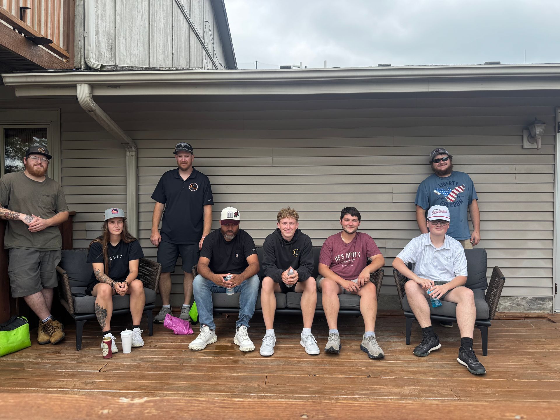 Group of eight people sitting and standing on a wet wooden deck in front of a garage door
