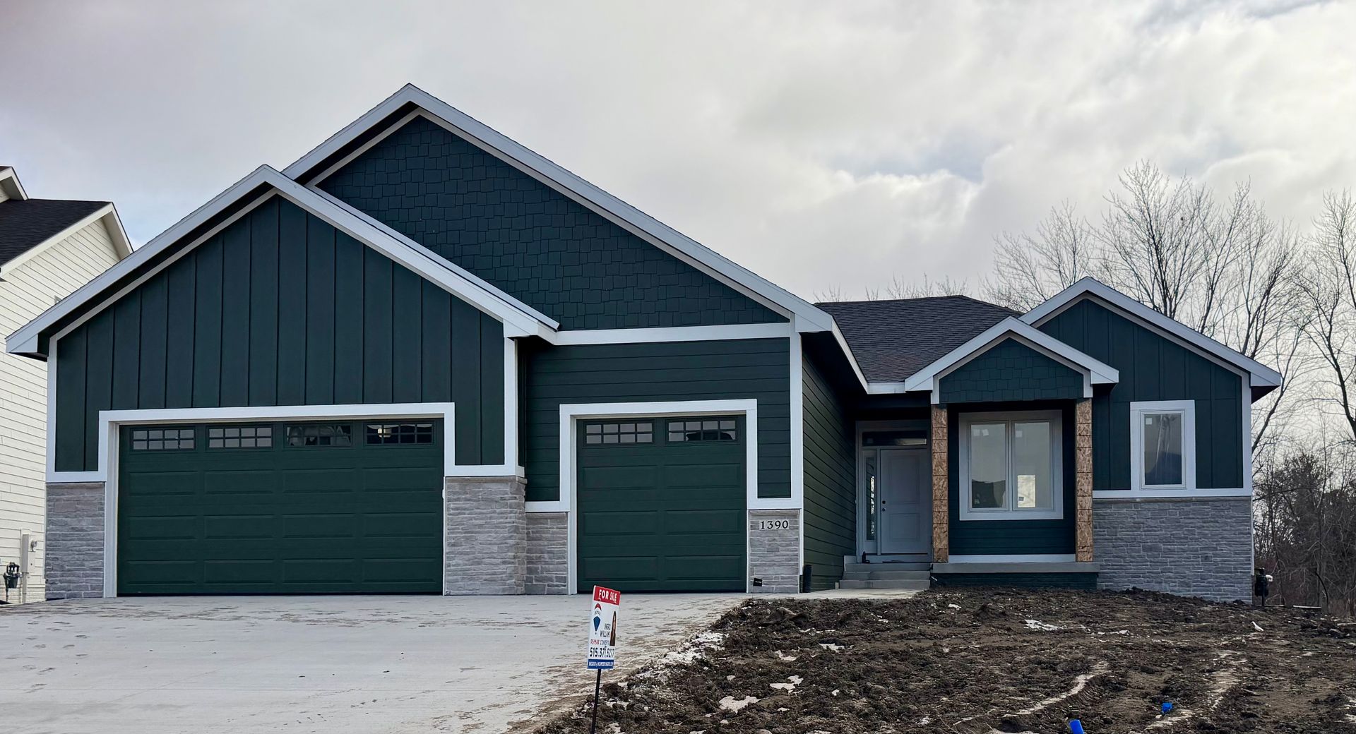A newly built, dark teal house with two-car garage, grey stone accents, and cloudy sky backdrop.