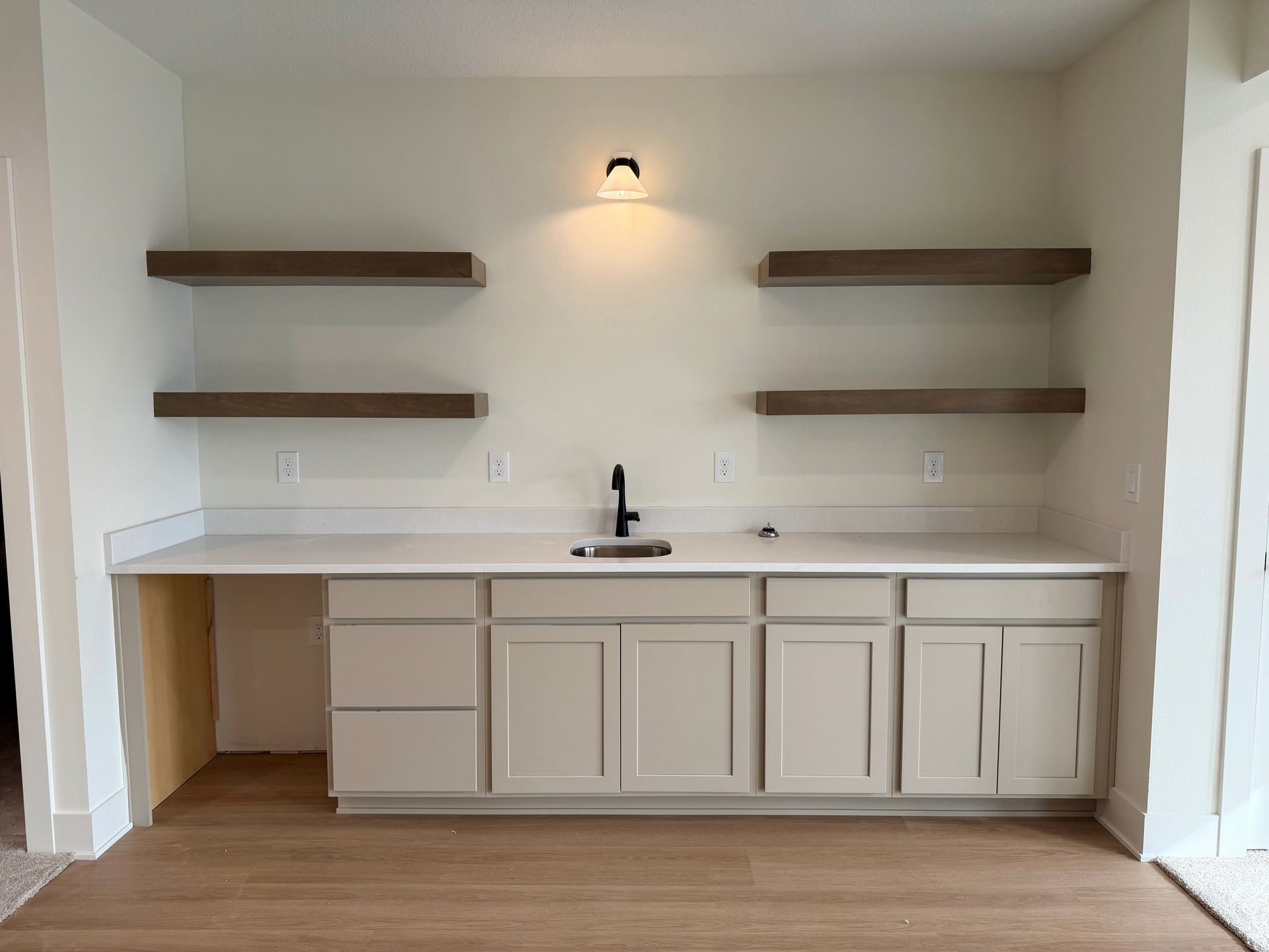 Built-in bar with floating shelves, light fixture, sink, cabinets, and countertop against a light wall.
