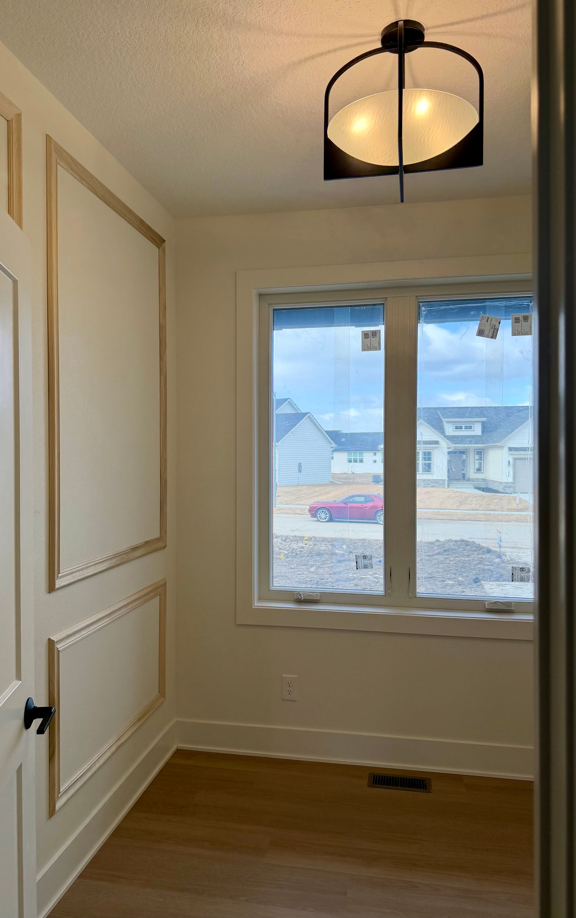 A small room with light-colored walls, molding, a window, and a hanging light fixture.