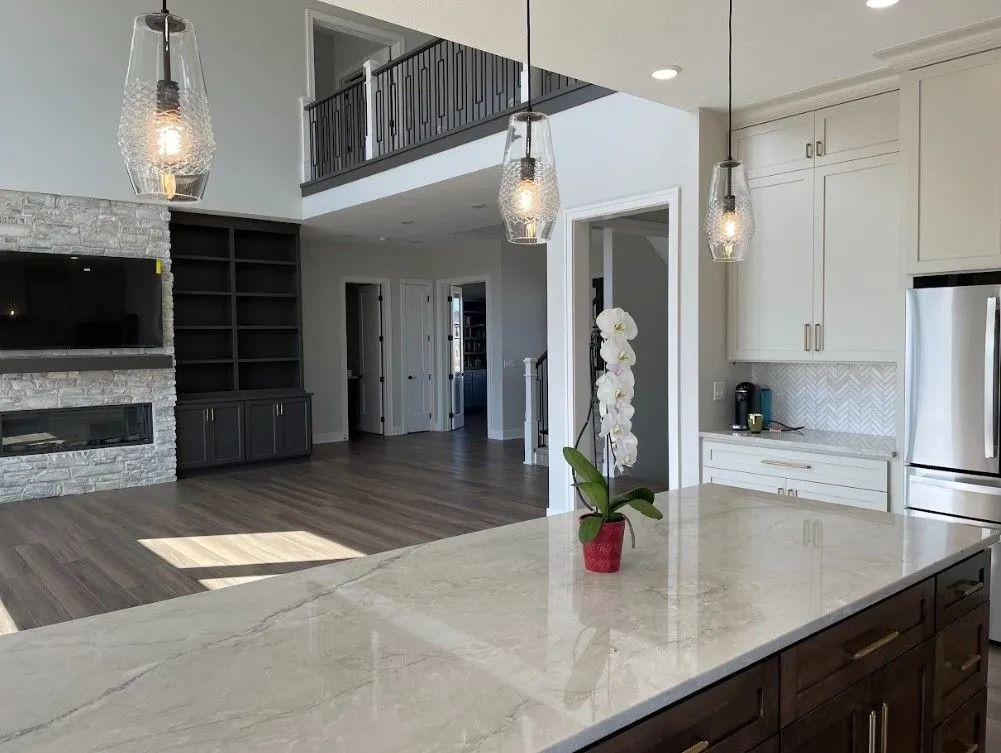 Modern kitchen with island, fireplace, and two-story living area. White and gray tones, wood floors, and decorative lighting.