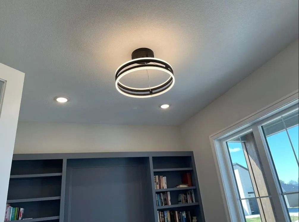 Modern circular ceiling light illuminates a room with built-in bookshelves and windows.