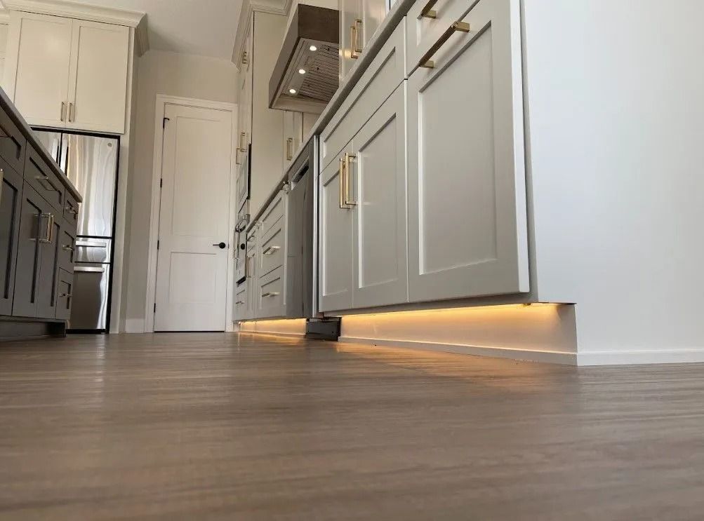 Kitchen cabinets with under-cabinet lighting. Light wood-look flooring and white walls.