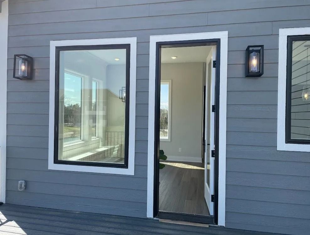 Exterior of a modern home with gray siding, black framed windows and door, and sconce lights.