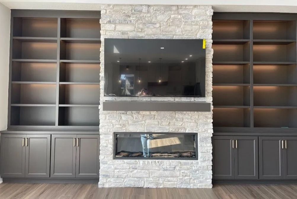 Built-in gray bookcase with TV and fireplace on a stone wall, against a light wood floor.