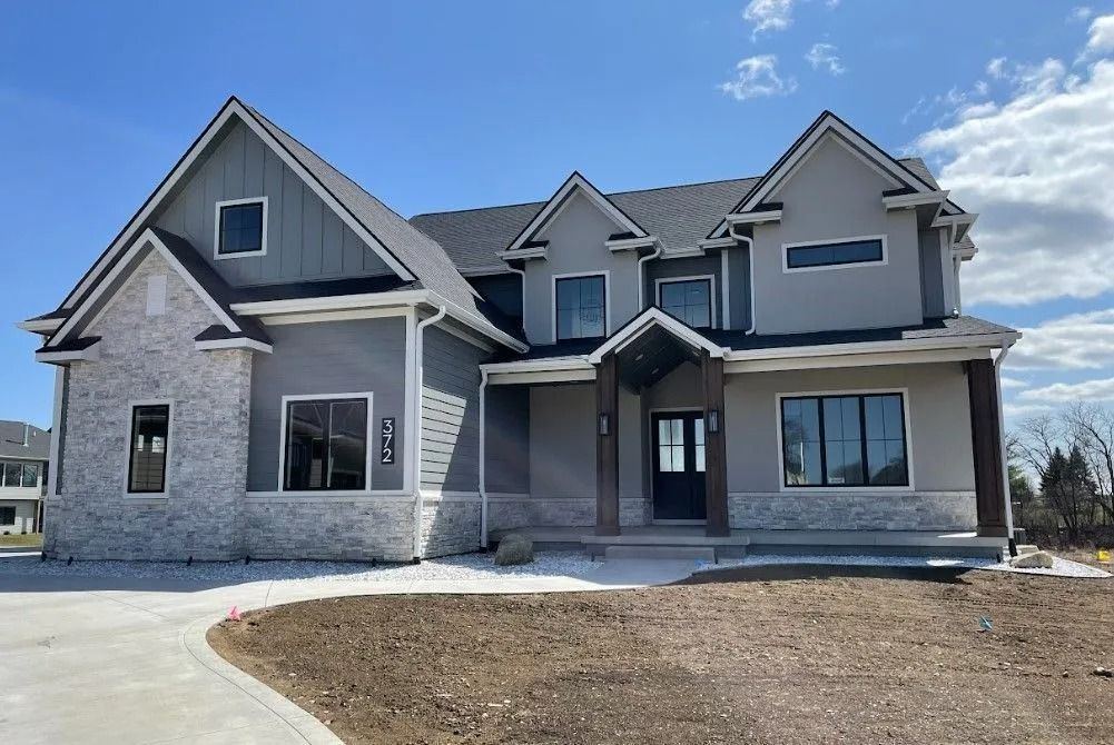 Two-story modern home with gray stucco, light stone accents, and dark roof under a blue sky.