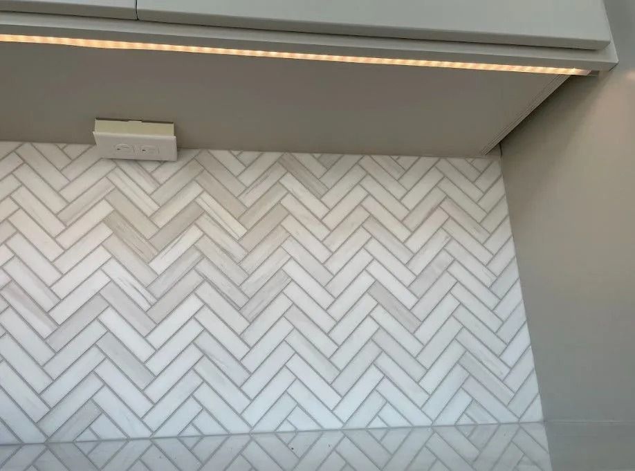 Herringbone tile backsplash below a cabinet with under-cabinet lighting.