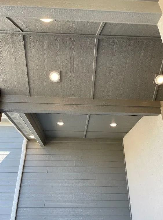 Gray porch ceiling with recessed lights and wooden beams. Gray siding on the wall below.