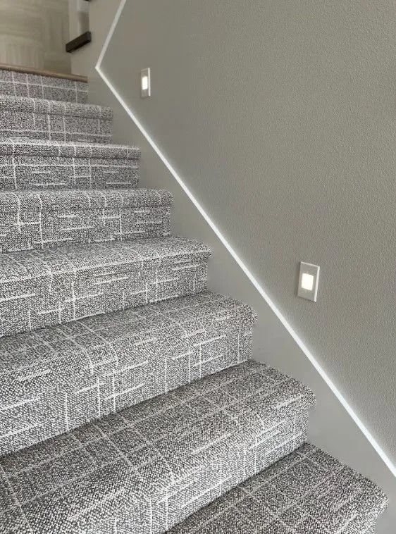 Staircase with gray patterned carpet and wall lighting.