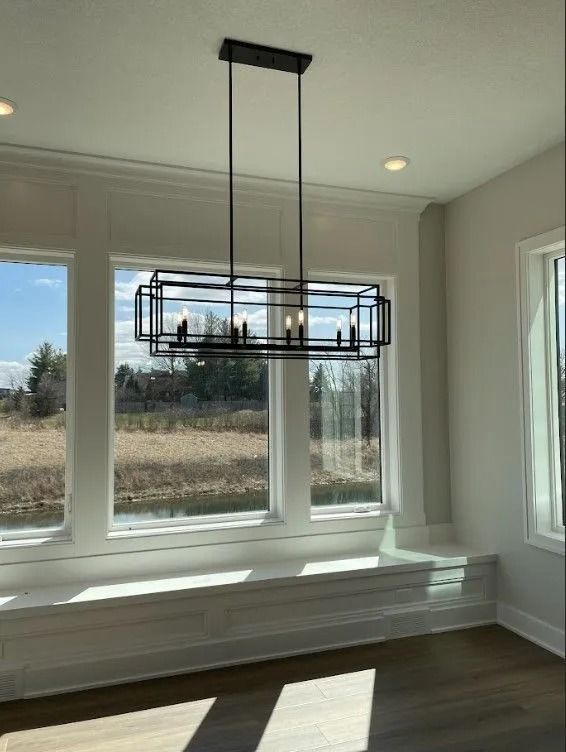 Modern black rectangular chandelier above windows, looking out at a field.