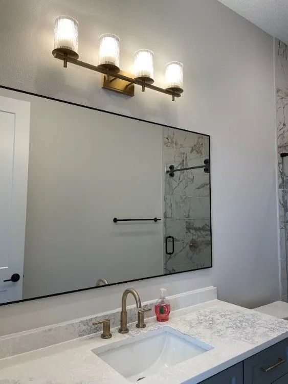 Bathroom with a rectangular mirror, gold light fixture, white countertop, and gray cabinets.