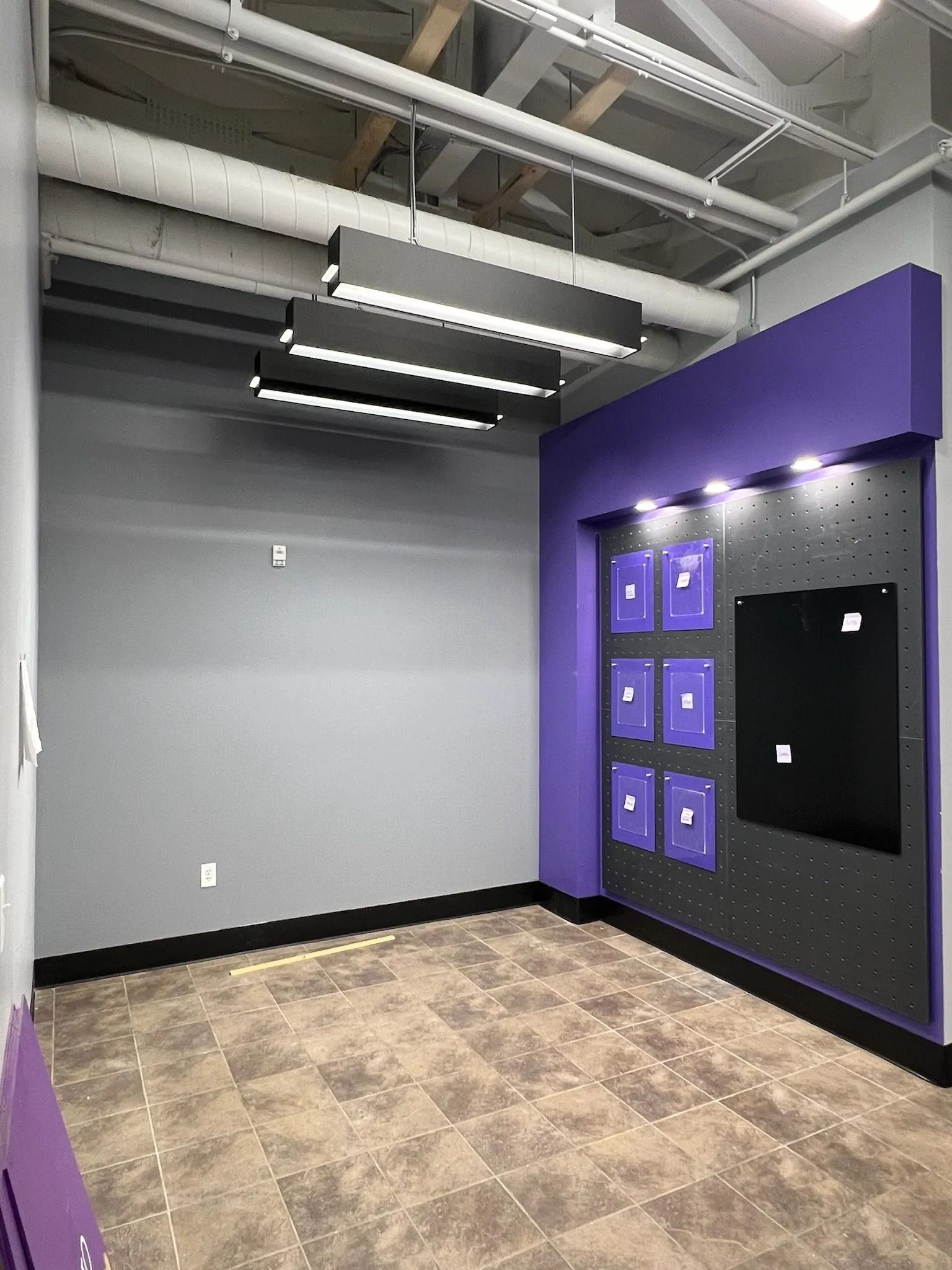 Empty room with gray walls, purple accent wall with display, and rectangular hanging lights.