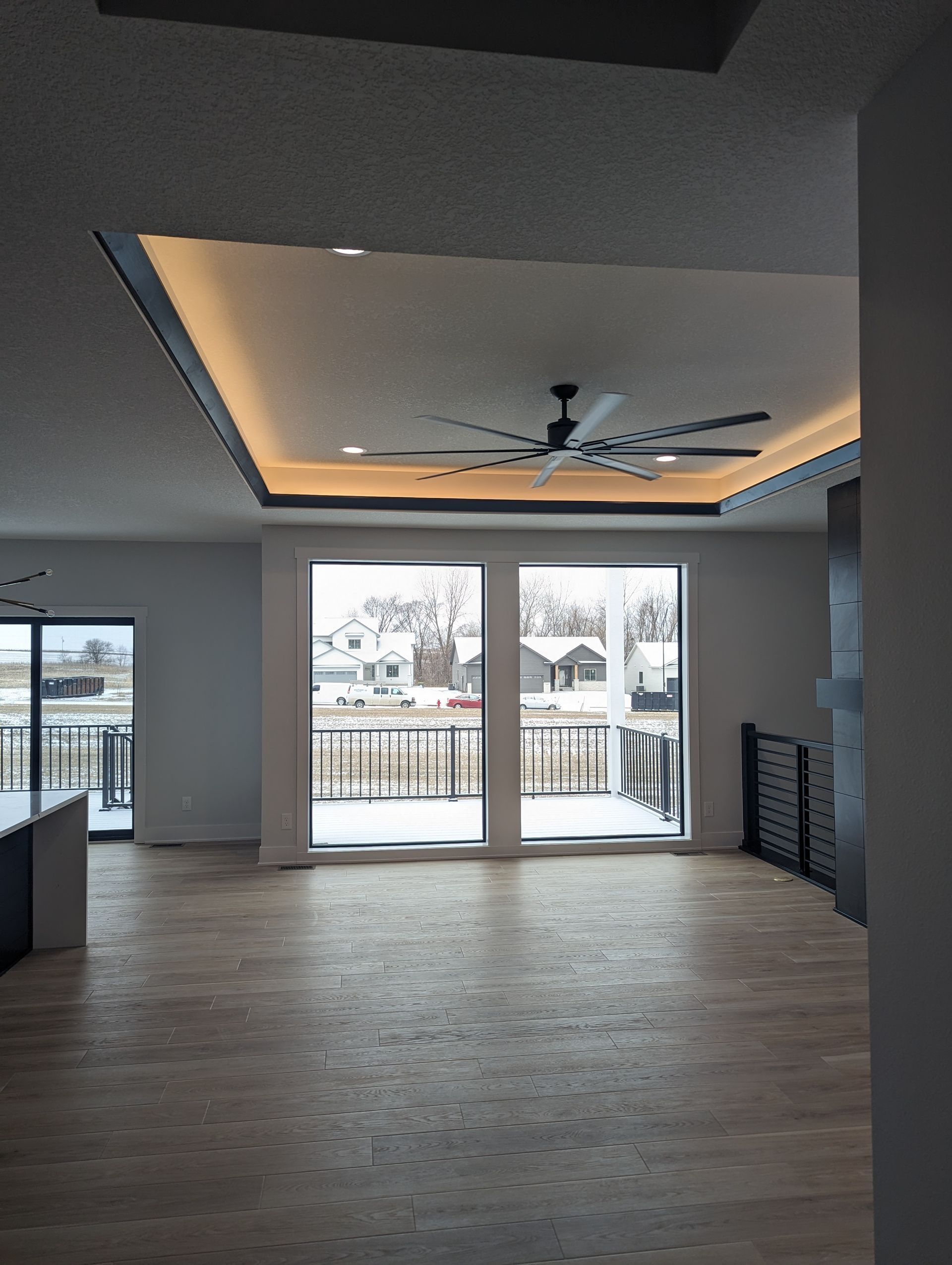 Modern living room with light wood floors, large windows, and a recessed ceiling with lighting.