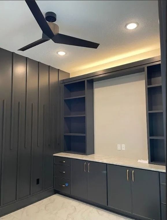 Dark gray home office with built-in cabinetry, bookshelves, and a ceiling fan.
