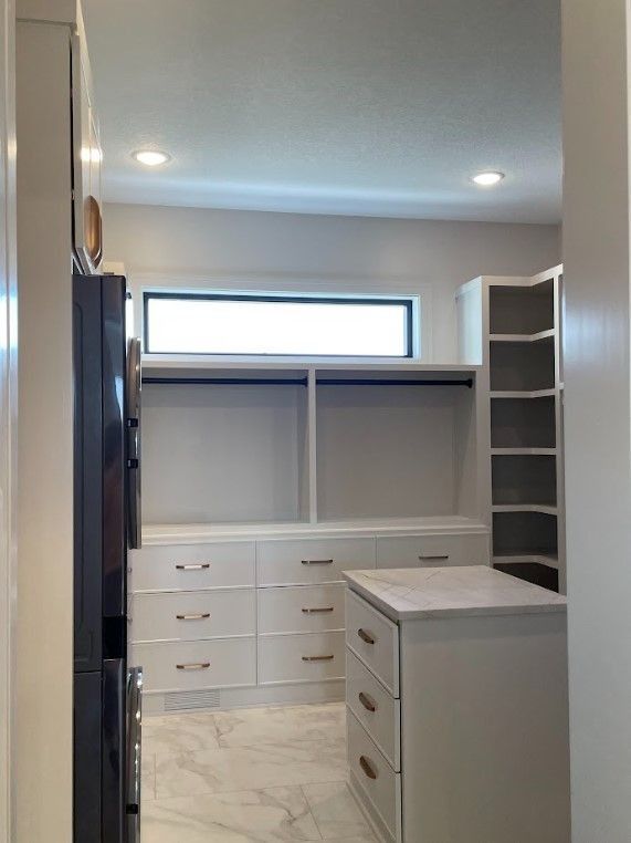 White walk-in closet with drawers, shelves, hanging rods, and a marble countertop. A small window provides natural light.