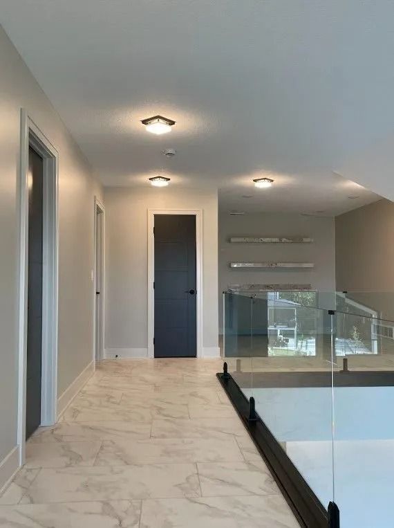 Hallway with marble floor, doors, glass railing, and overhead lighting.