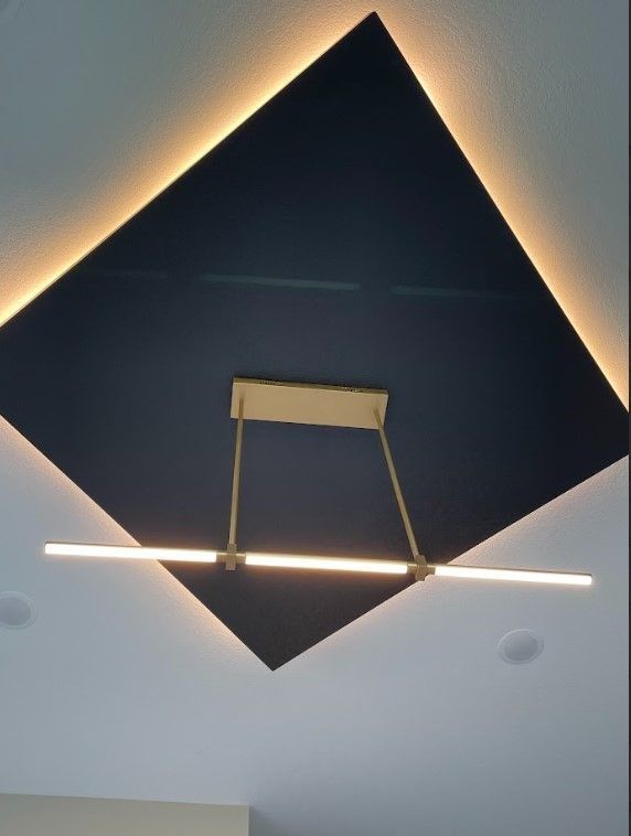 Gold light fixture hangs below a navy blue diamond-shaped ceiling panel with perimeter lighting.
