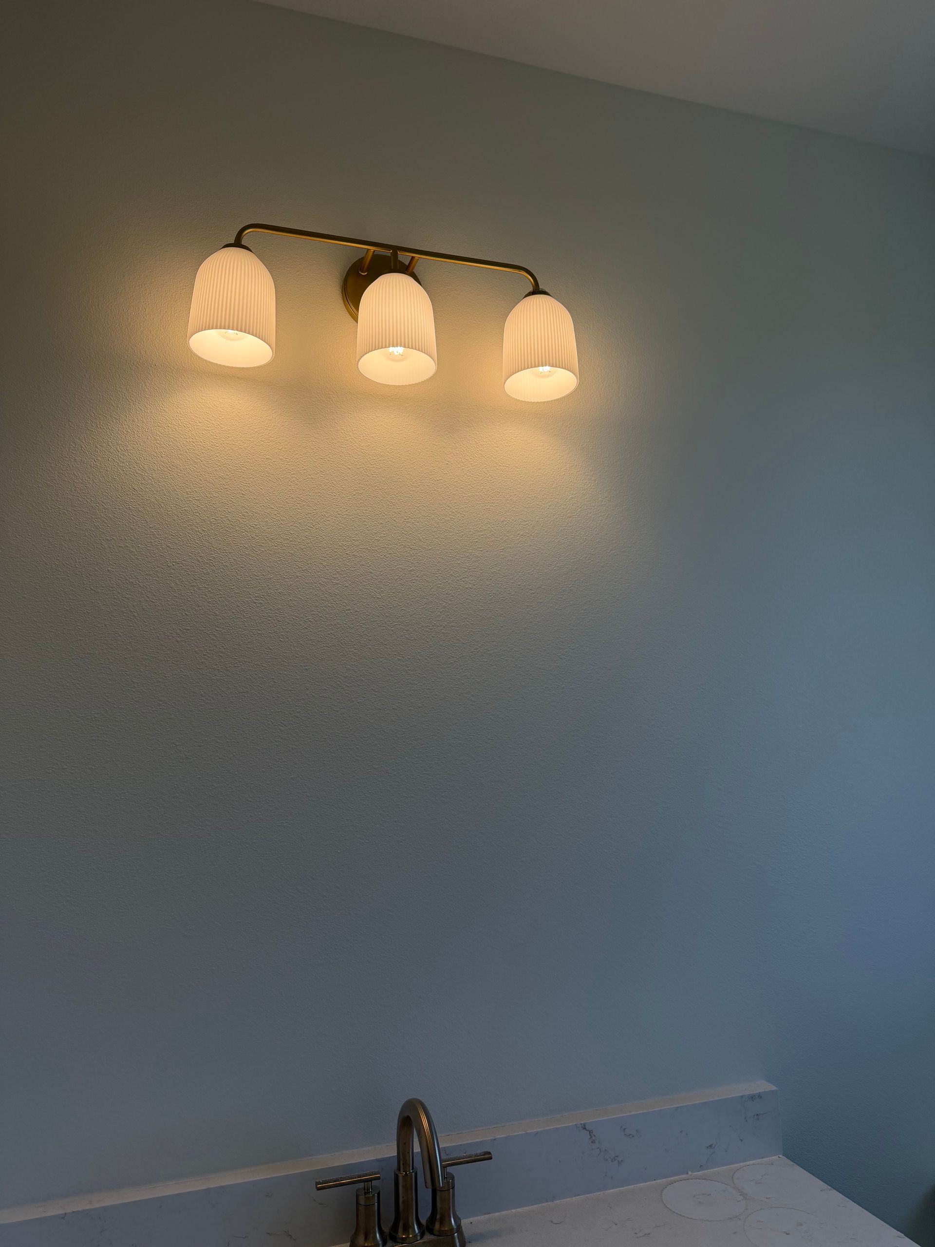 Bathroom wall with three lit vanity lights above a sink and mirror edge