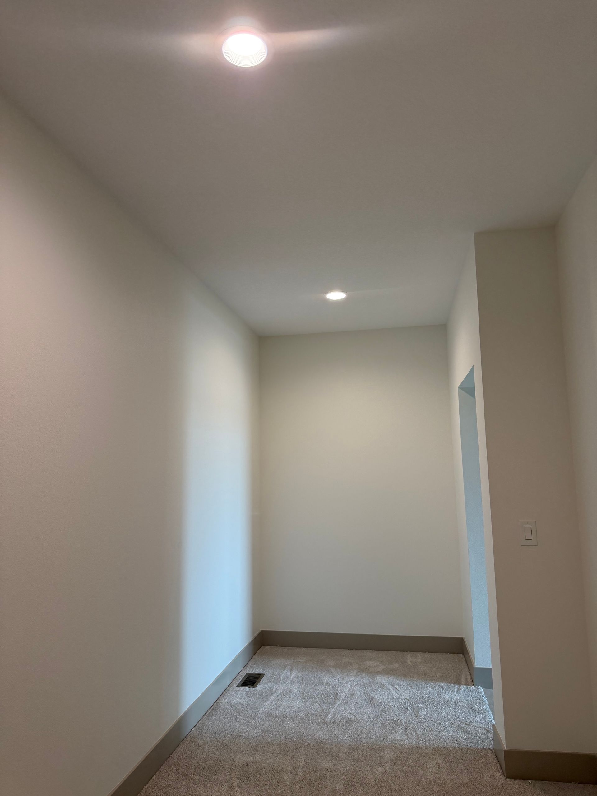 Empty hallway with white walls, recessed lights, and carpeted floor leading to a doorway.