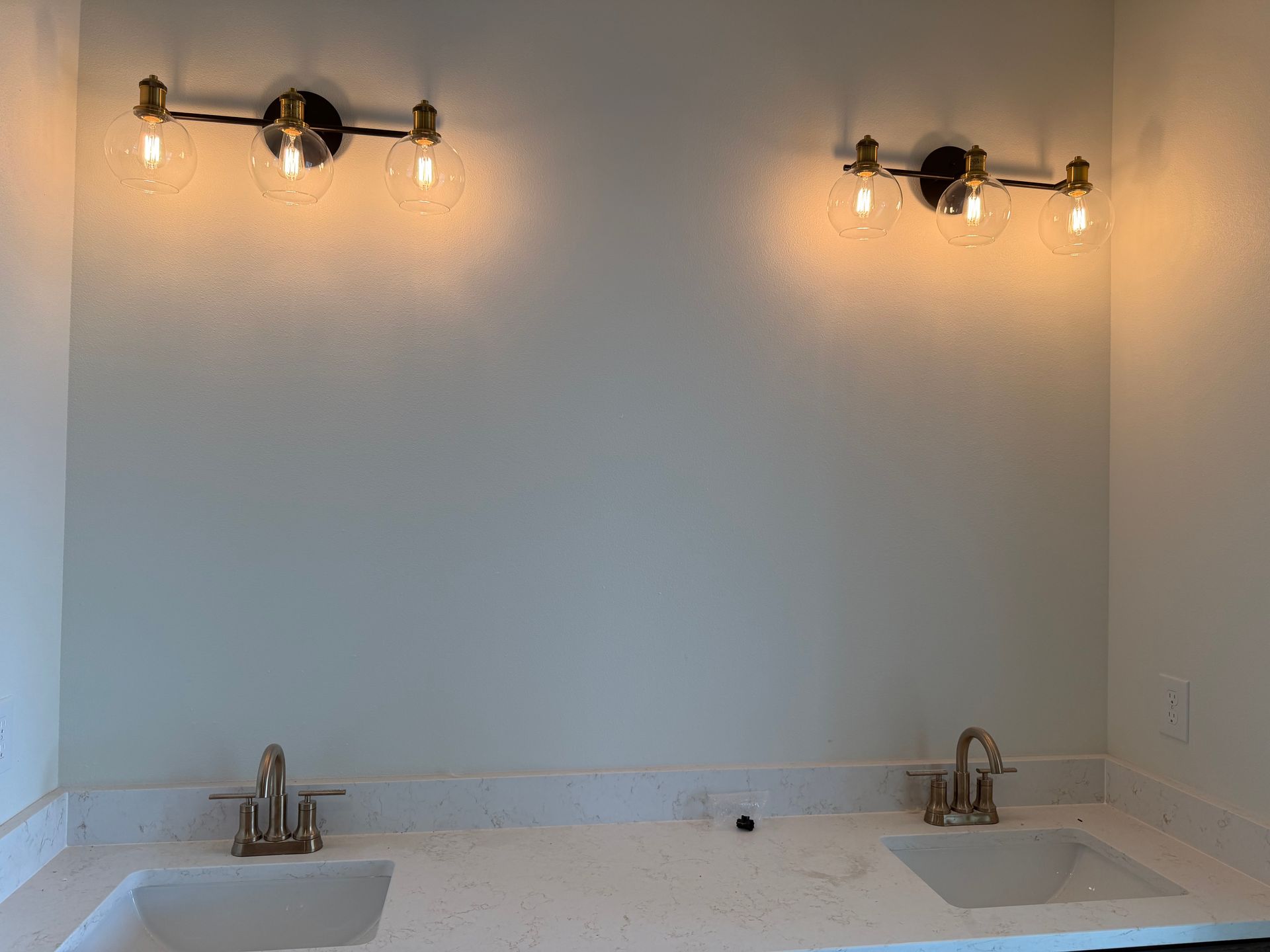 Empty double-sink vanity with wall sconces and a large mirror in a bright bathroom.
