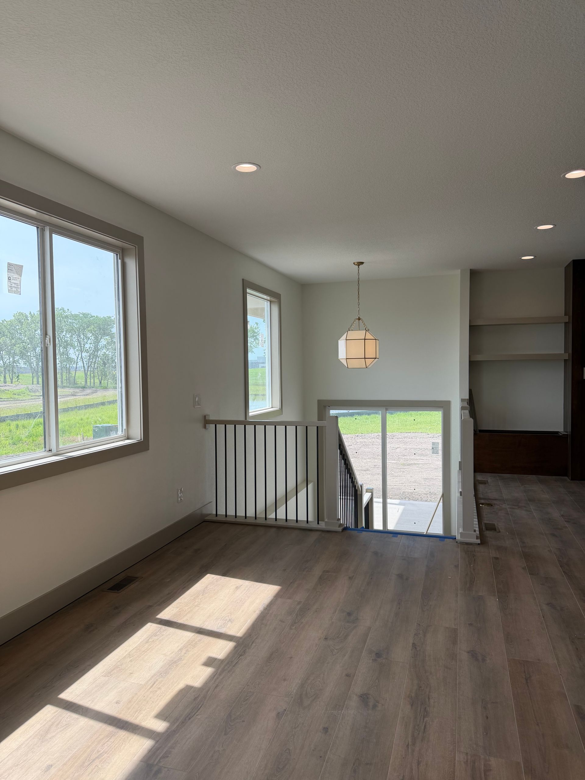 Bright empty room with wood floors, white walls, windows, and a stair landing overlooking outdoors