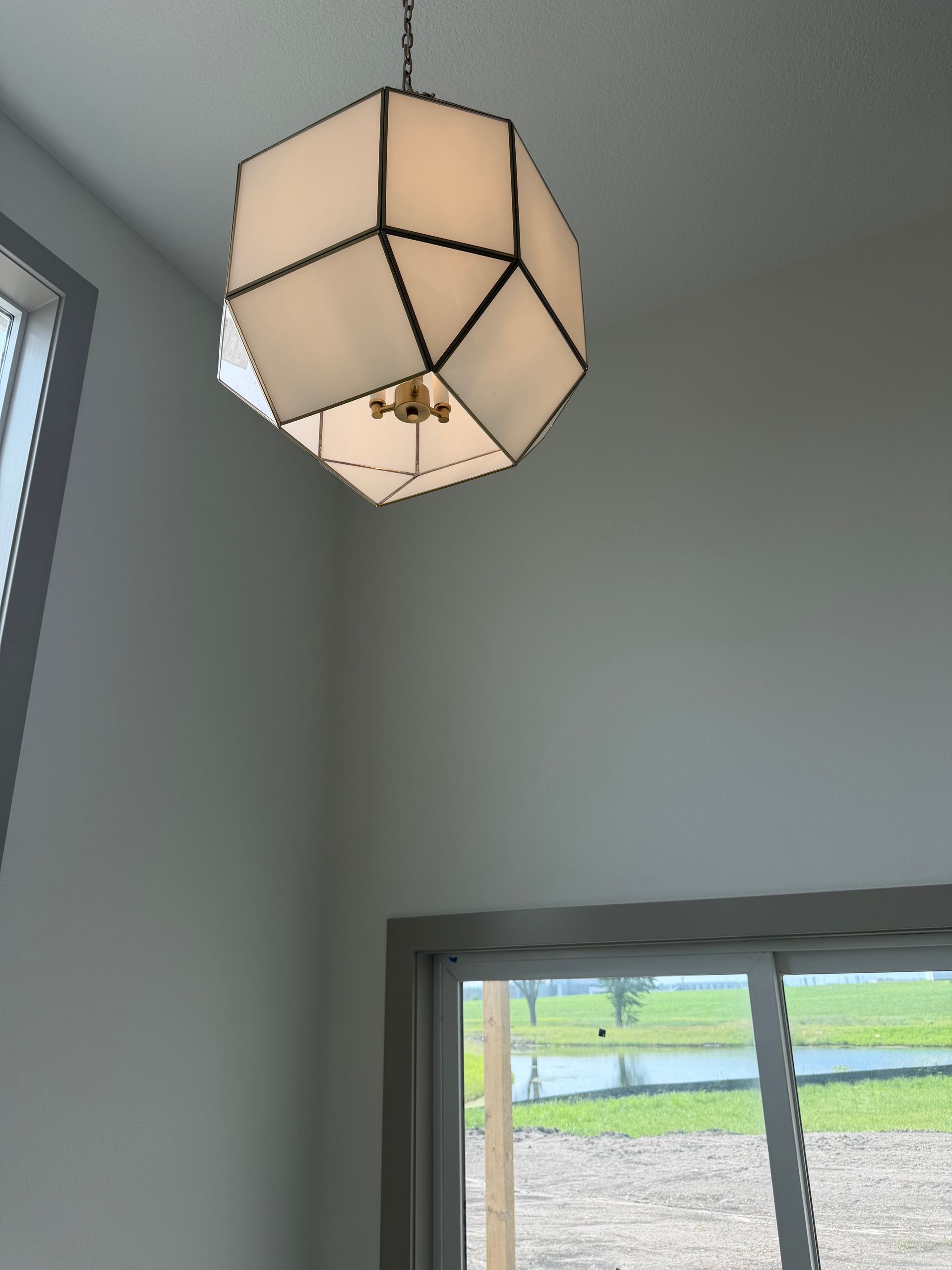 Ceiling light with beige geometric shade in a room above a window and gray walls