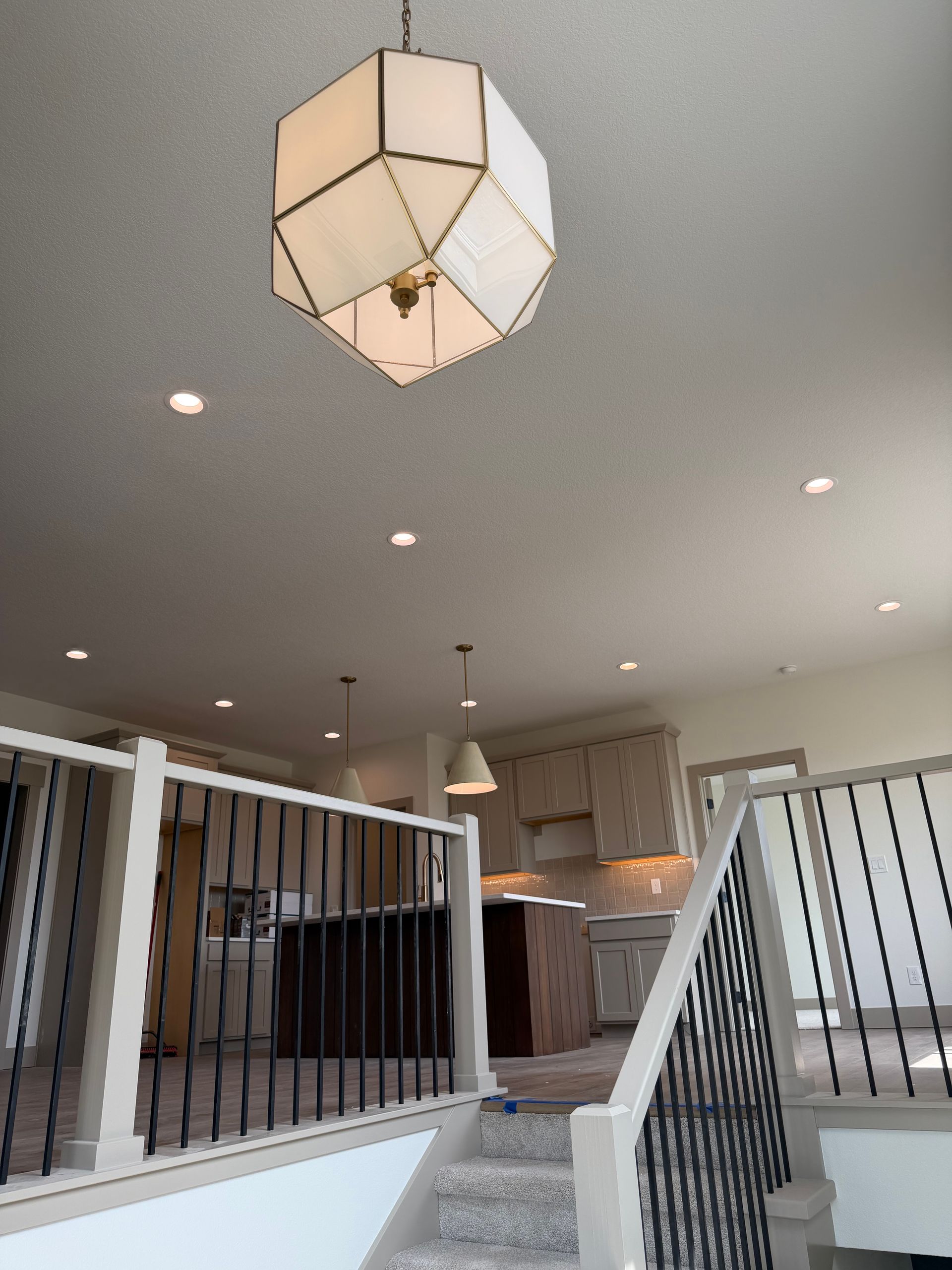 Modern foyer with geometric pendant light, recessed ceiling lights, and stair railings leading to a living area