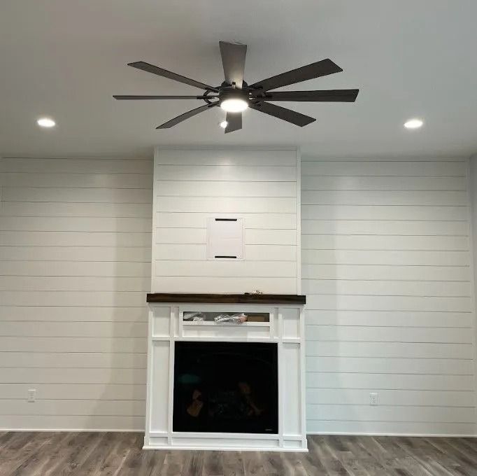 Living room with fireplace, white shiplap walls, dark ceiling fan, recessed lights, and dark wood floor.