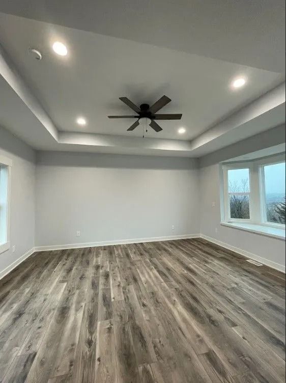 Empty room with light gray walls, dark wood-look flooring, recessed lighting, and a dark ceiling fan.