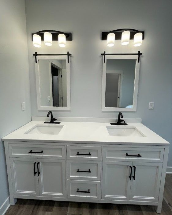 White double bathroom vanity with black hardware, light fixtures, and mirrors on light blue wall.