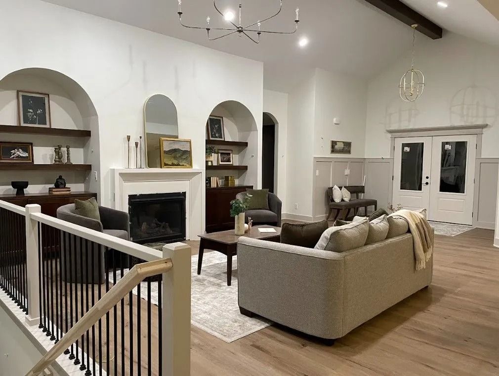Living room with arched fireplace, shelves, sofa, chairs, and wood floors.