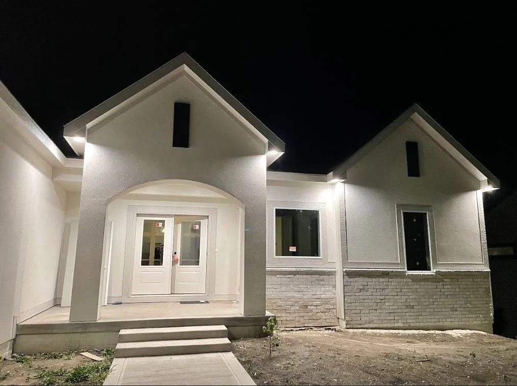 White house exterior lit at night, with multiple gabled sections, front door and steps.