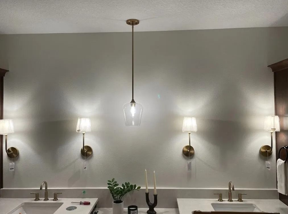 Bathroom with light fixtures: pendant light, two sconces on each side of sinks. Beige walls, white countertops.