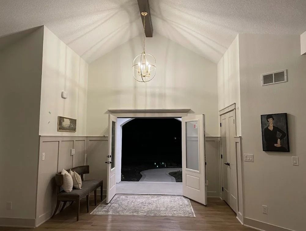 Interior view of a light-filled entryway with open double doors leading to a dark outdoor space.
