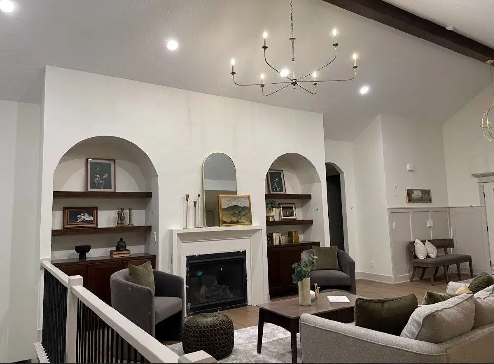 Living room with fireplace, arched shelves, and modern chandelier. Neutral tones with dark furniture.